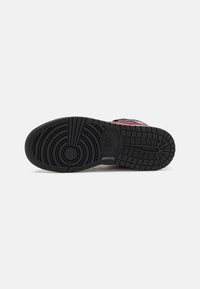 Black rubber sneaker sole with a textured design, featuring circular patterns and horizontal grooves for traction. Red accents near edges.