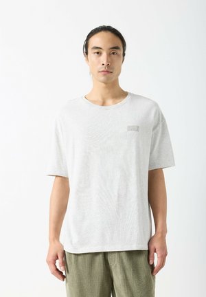 Svetlo siva bombažna majica z okroglim izrezom, kratkimi rokavi in subtilnim logotipom "AMERICAN VINTAGE" na prsih. Mehka tekstura.