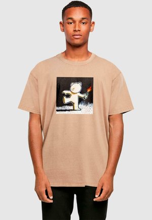 Beige cotton t-shirt featuring a central graphic of a white bear holding a burning object, set against a dark background. Short sleeves.