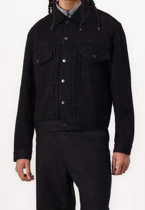 Veste en jean noire avec fermeture à boutons, deux poches poitrine et design légèrement raccourci. Tissu texturé avec une silhouette structurée.