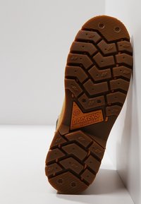 Brun gummistøvle sål med dybe riller og "DOCKERS FOOTWEAR" logo prægede i midten.