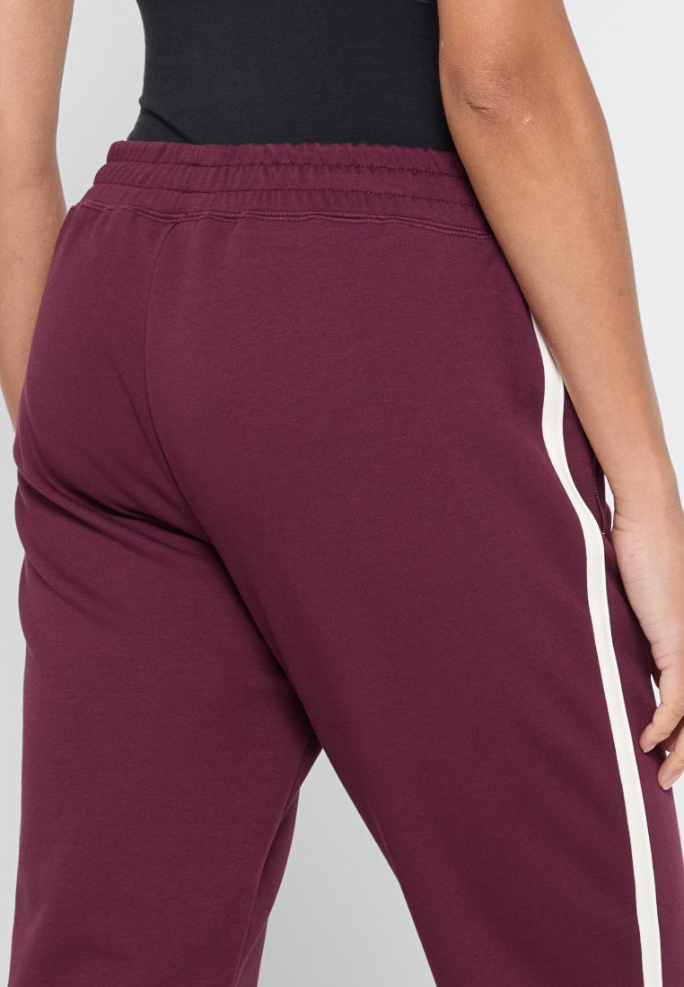 Joggers burdeos con una textura suave, que cuentan con una franja lateral blanca. Cintura elástica para un ajuste ajustable. Diseño simple y casual.