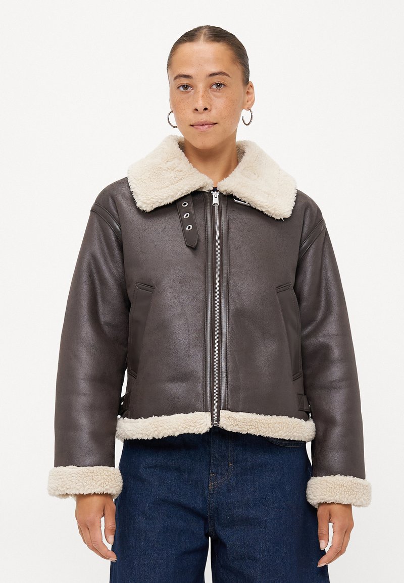 Giacca in finta pelle marrone con un morbido colletto e polsini in sherpa color crema. Presenta una zip frontale, tasche laterali e un design corto.