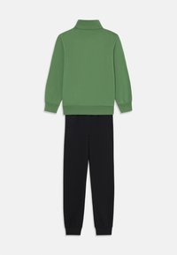 Sudadera verde con cuello alto y mangas largas combinada con pantalones jogger negros. Ambas prendas tienen una textura suave y un corte relajado.