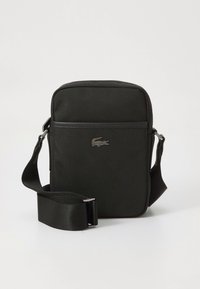 Musta keinonahkainen olkalaukku, suorakulmainen muoto, sileä pinta, säädettävä hihna ja metallinen logokoriste edessä.