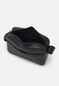 Czarna skórzana torba na ramię z pikowaną fakturą, zamkiem błyskawicznym i przestronnym wnętrzem. Posiada szeroki pasek i minimalistyczny design.