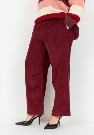 Burgundy corduroy trousers with a straight cut, featuring side pockets and a textured finish, paired with black pointed high heels.
