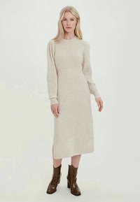 Μπεζ ριπ πλεκτό φόρεμα με μακριά μανίκια, στρογγυλή λαιμόκοψη και πλαϊνές σχισμές, σε συνδυασμό με καφέ υφή μποτάκια μέχρι τον αστράγαλο.