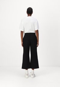 Fekete, bő szárú nadrág magas derékkal, fehér, rövid ujjú pólóval párosítva. A modellen fehér sportcipő van, látható bokazoknival.