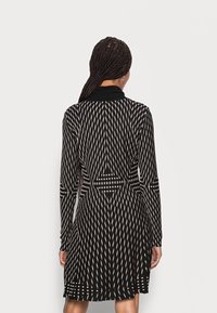 Langärmliges Kleid in Schwarz mit einem weißen geometrischen Muster. Verfügt über einen Kragen und eine taillierte Taille, mit einem schwingenden Rock, der bis zur Mitte des Oberschenkels reicht.