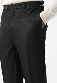 Schwarze Hose aus einem glatten, fein strukturierten Stoff. Verfügt über eine schlanke Passform, vordere Taschen und einen Schnallenverschluss an der Taille.