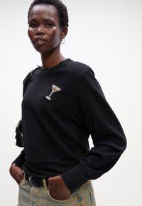 Sudadera negra con un diseño de copa de martini con cuentas en el pecho. Mangas largas, cuello redondo y una tela texturizada.