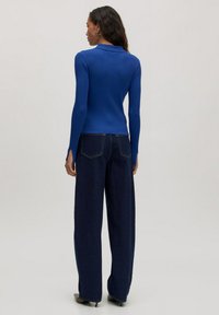 Blauwe geribde blouse met lange mouwen en kraag, gecombineerd met high-waisted donkerdenim wijde broek met twee achterzakken en stiksels.
