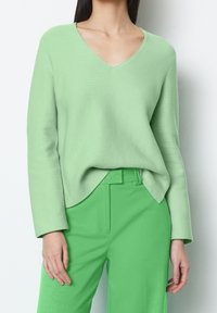Light green, V-neck sweater made of a textured knit fabric, paired with bright green tailored pants featuring a flat front and side pockets.