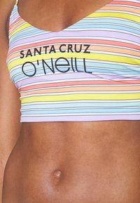 Top corto a righe con linee lavanda, rosa, blu, arancione e giallo. Presenta un design a V e testo del logo nero in grassetto. Tessuto morbido al tatto.