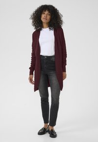 Cardigan en maille bordeaux à manches longues, ouvert à l'avant, avec un motif texturé, associé à un jean skinny noir et des mocassins noirs.
