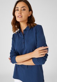 Marineblauwe lange mouw polo shirt met kraag, drie knoppen sluiting en ribgebreide cuffs. Heeft een licht gebogen zoom en een zachte textuur.