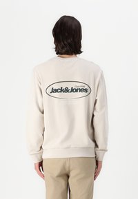 Bežinis vilnonis megztinis su dideliu juodu oviniu logotipu "Jack&Jones" ant nugaros. Ilgos rankovės su elastiniais rankogaliais ir apačia. Lygus audinio paviršius.