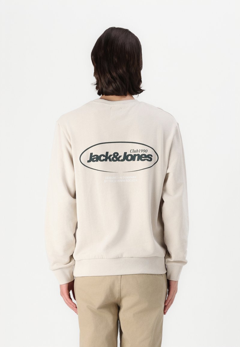 Sudadera beige con un gran logo ovalado negro "Jack&Jones" en la parte posterior. Mangas largas con puños y dobladillo acanalados. Textura de tejido suave.