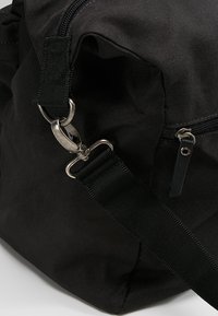 Sac en tissu noir avec quincaillerie en argent, doté d'une fermeture éclair, d'une bandoulière ajustable et d'un clip en métal. Matériau texturé avec des accents cousus.