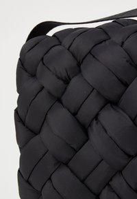 Borsa nera intrecciata caratterizzata da una texture trapuntata morbida, con una finitura in tessuto liscio e una sottile tracolla piatta.