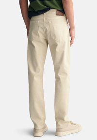 Beige bomullblandede chinos med rett passform, som har to baklommer og et brunt lærbelte. Uformell, allsidig design.