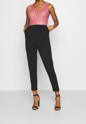 Rosa v-hals krop med tilpasset talje, der går over i sorte, tilspidsede bukser. Modellen bærer sorte hæle med stropper, hvilket fremhæver en slank silhuet.