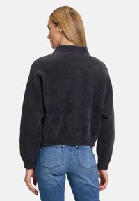Maglione peloso grigio scuro con colletto alto e spalle basse, abbinato a jeans di denim azzurri. Presenta un design cropped.