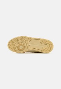 Sneaker sole in beige rubber with circular patterns and horizontal grooves, featuring Adidas branding. Textured for grip and support.