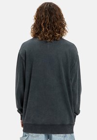 Sudadera de gran tamaño en gris oscuro, confeccionada con un tejido suave, que presenta un cuello redondo y puños acanalados. La vista trasera muestra un ajuste relajado.