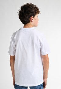 Camiseta blanca de algodón con mangas cortas y cuello redondo, mostrada desde la parte de atrás. La tela parece suave, sin patrones visibles.