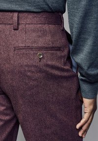 Burgunderfarbene Wollhosen zeichnen sich durch eine glatte Textur, eine Gesäßtasche mit Knopf und ein sauberes, maßgeschneidertes Design aus, ergänzt durch einen grauen Pullover.
