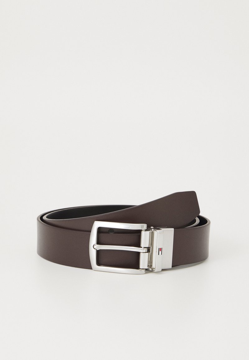 Barna szintetikus öv ezüst fém csattal, téglalap alakú és sima textúrával rendelkezik. A csat finom logóelemmel van ellátva.