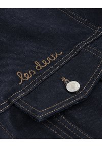 Tessuto di denim blu scuro con cuciture dorate, con il testo ricamato "les deux" e un dettaglio in argento sul taschino.