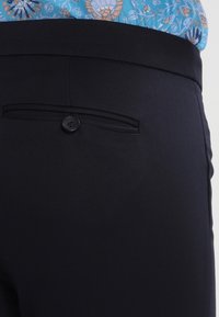 Svarta byxor med en elegant design, mjuk textur och en bakficka med knapp. Midjan är skräddarsydd för en figurnära look.