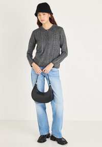 Sivi rebrasti kardigan z gumbi, svetlo modre jeans hlače in majhna črna usnjena torbica. Črna pletena kapa in masivne črne čevlje.