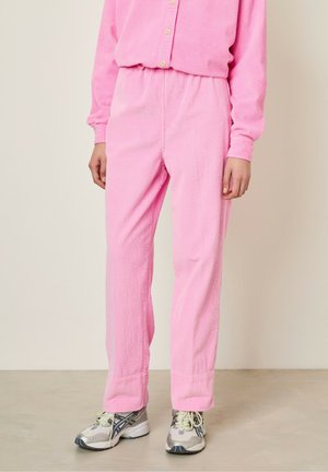 Pink corduroy pants with an elastic waist, straight leg design, and textured fabric. Paired with gray athletic shoes.