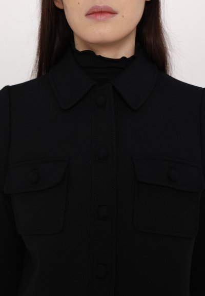 Black shirt with a collared neckline, featuring two chest pockets, button closure, and textured fabric. Smooth surface with no patterns.