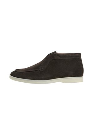 Donkerbruine suède enkellaars met witte zool en mocassinstijl stiksels, zijaanzicht op een witte achtergrond.