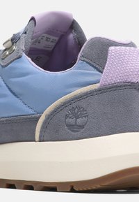 Blå och grå sneaker med överdel i mocka och nylon, texturerade lila accenter, vadderad krage och en gummisula med en trädlogotyp.