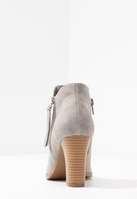 Botín de ante gris con tacón apilado, con cremallera lateral y detalle de borlas. Textura suave y diseño de punta redondeada.