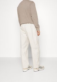 Ljusbeiga byxor med loose fit, elastisk midjeband och fickdetaljer, tillsammans med beiga sneakers med mörka accenter.