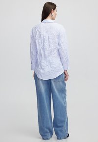 Camicia bianca con righe verticali blu, caratterizzata da una vestibilità comoda e maniche lunghe, abbinata a jeans in denim blu larghi.