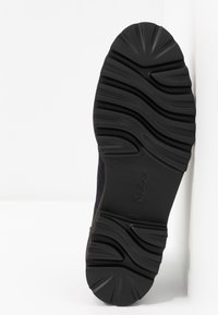 Schwarze Gummisohle mit welligem Profil, leicht gebogen an der Spitze und strukturiertem Oberflächenmaterial für besseren Halt. Minimalistisches Design.