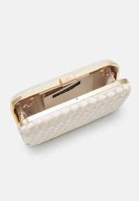 Kutomoitu satiininen clutch-laukku, jossa on kullanvärinen metallikehys, ketjuhihna ja beige sisusta. Laukussa on myös etiketti ja tasku.
