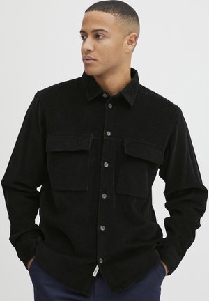 Black corduroy shirt with two chest pockets, long sleeves, and button front. Features vertical ribbed texture and a classic collar.