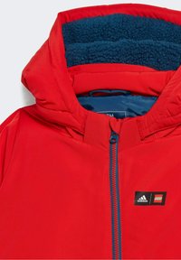 Chaqueta acolchada roja con forro de forro polar azul, cremallera frontal y logotipos de Adidas y LEGO en el pecho.