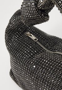 Bolsa de mão preta coberta de pequenas pedras de strass facetadas. Apresenta um fecho com zíper e uma alça torcida, refletindo a luz da sua superfície texturizada.