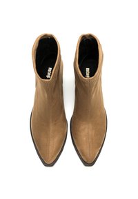 Un par de botas de tobillo de ante color beige con punta afilada, con plantillas negras y costuras visibles, vistas desde arriba sobre un fondo blanco.