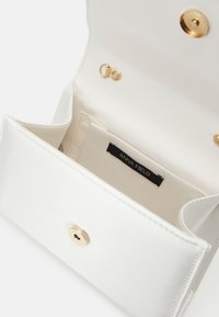 Porte-monnaie blanc ouvert avec fermoir doré et maillons de chaîne, poche intérieure étiquetée "Anna Field," montrant un design simple et épuré.
